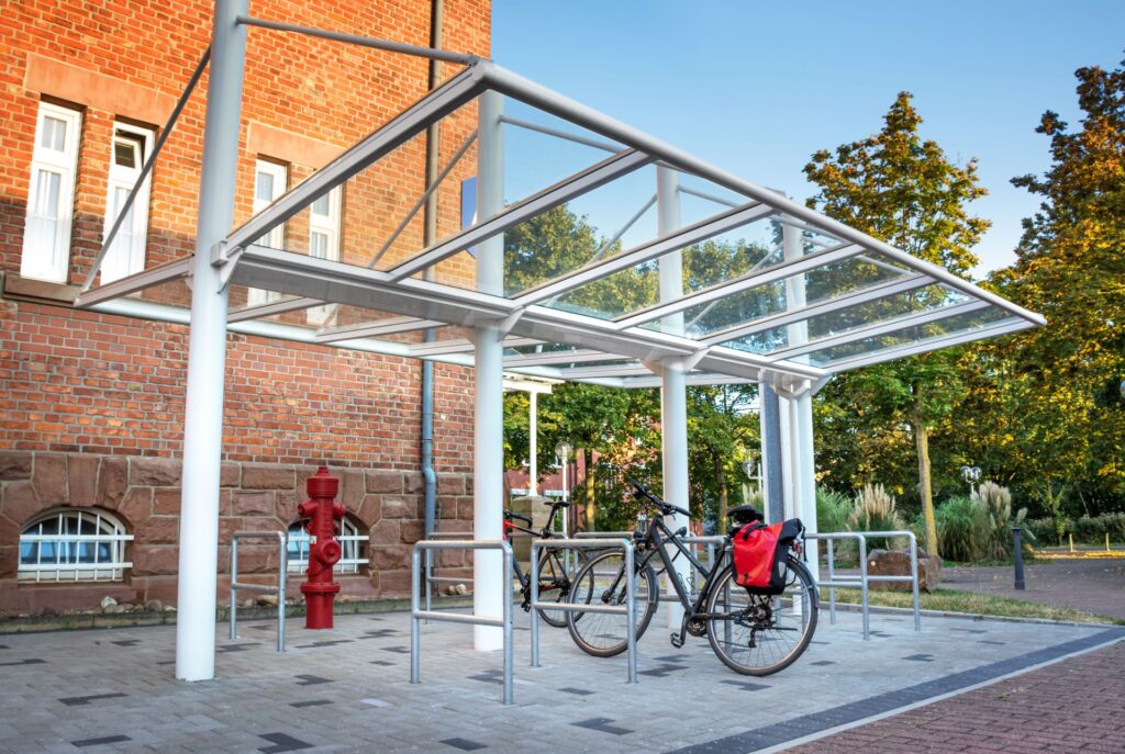 Fahrradüberdachung mit Glasdach und Fahrradständern vor einem Firmengebäude, bietet Mitarbeitern sicheren und wettergeschützten Abstellplatz.