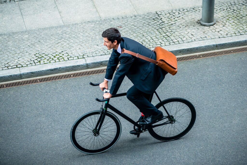 Ein Geschäftsmann in Anzug fährt mit dem Fahrrad zur Arbeit, eine Aktentasche über der Schulter, und zeigt den Trend zur nachhaltigen Mobilität im Berufsalltag