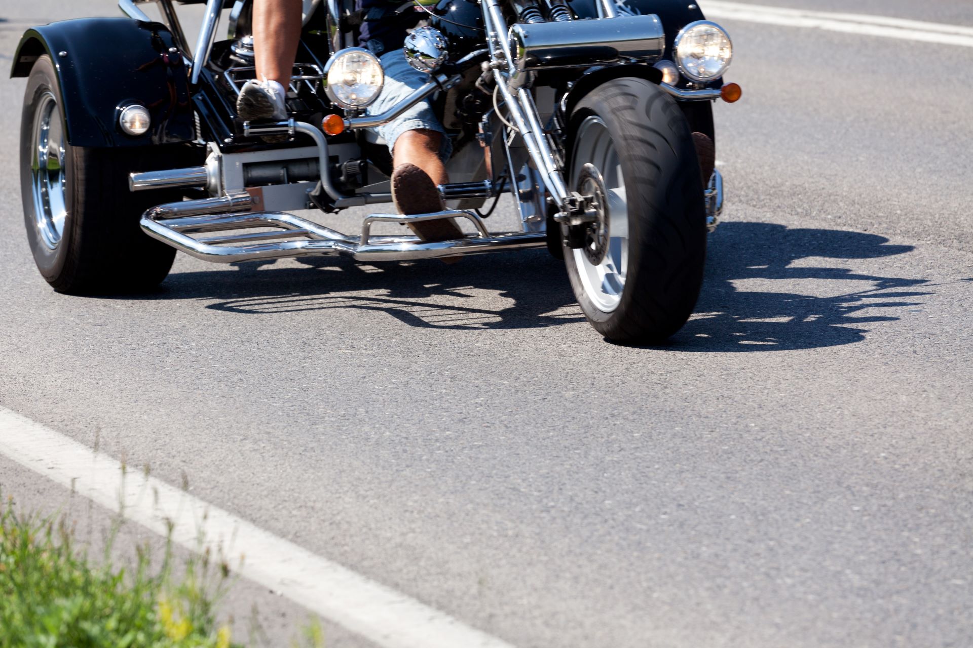 Nahaufnahme eines fahrenden Trikes auf einer Landstraße mit sichtbarem Vorderrad und Pedalen