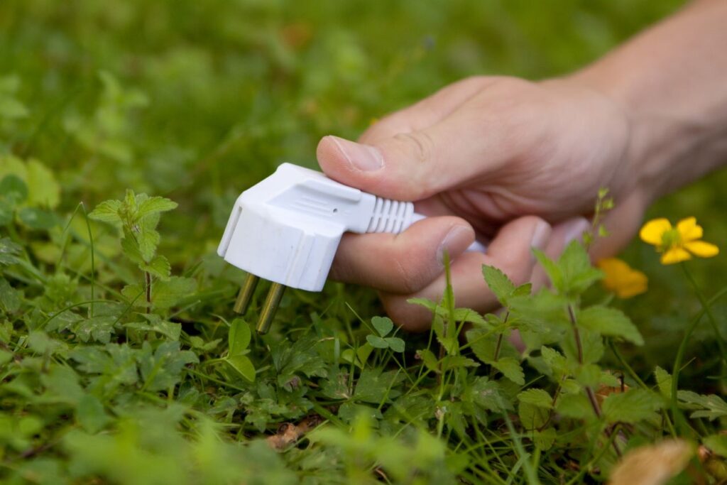 Hand hält einen Stromstecker auf einer grünen Wiese – Symbol für nachhaltige Energie und stromsparende Technologien wie LED-Strips.