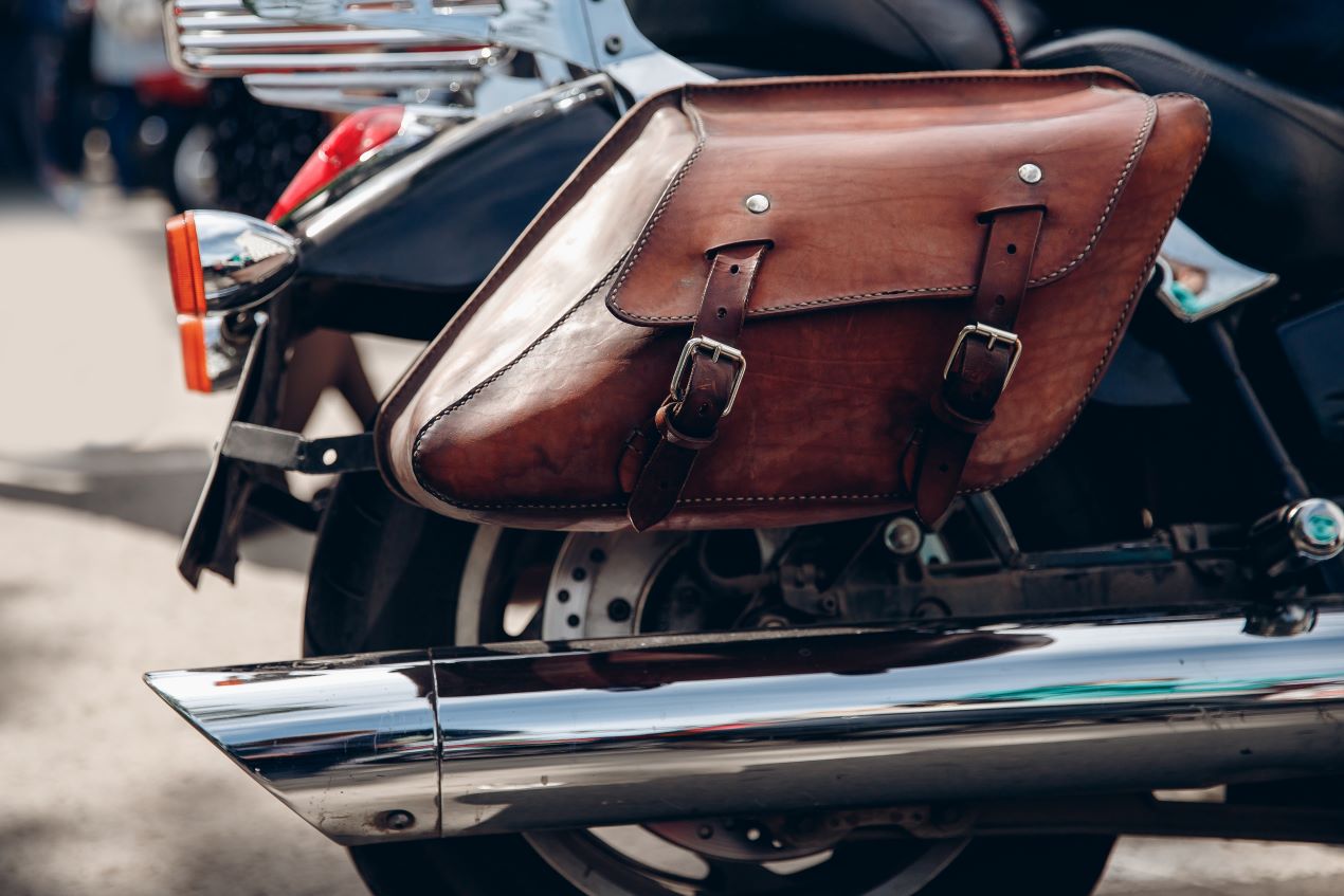 Nahaufnahme einer braunen Ledersatteltasche an einem schwarzen Motorrad, montiert oberhalb des Auspuffs als klassische Gepäcklösung.