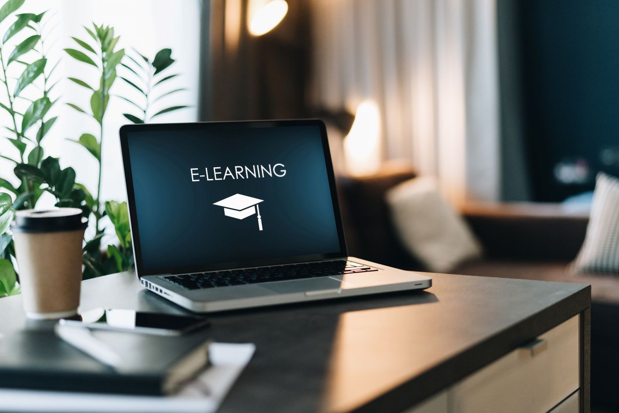 Ein Laptop zeigt das Wort „E-Learning“ mit einem Doktorhut-Symbol, ideal für Arbeitsschutz E-Learning in moderner Umgebung.