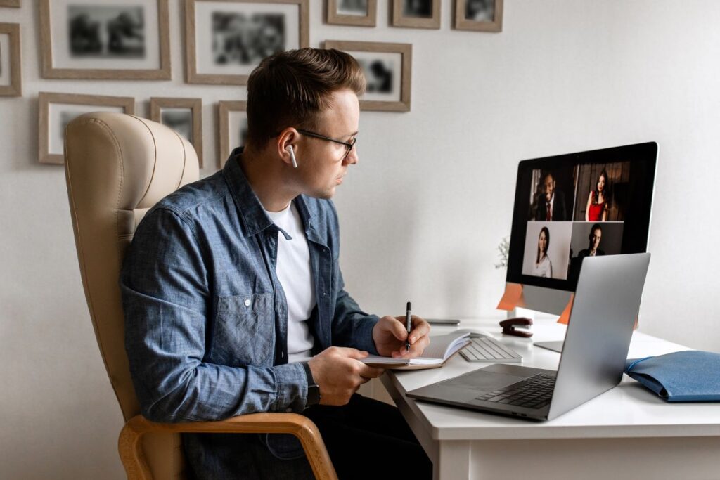 Ein Mann sitzt am Schreibtisch und nimmt an einer Videokonferenz teil, während er Notizen für ein Arbeitsschutz E-Learning macht.