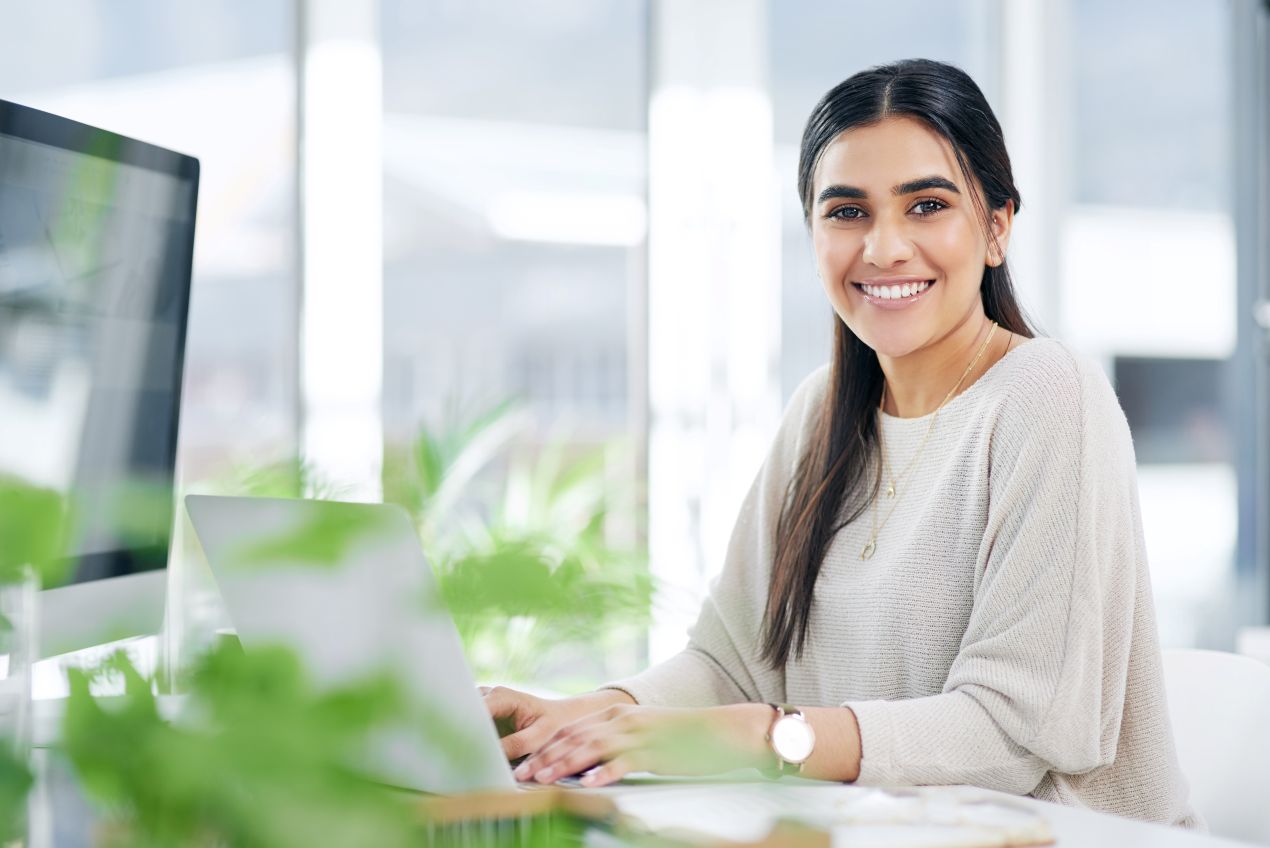 Eine junge Frau arbeitet an einem Laptop in einem hellen Büro, lächelnd während eines Arbeitsschutz E-Learning-Kurses.