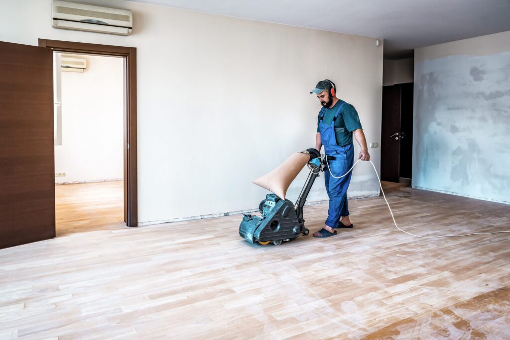 Professioneller Tischler, Arbeiter, Schleifen, Schleifen und Schleifen von Holzparkettböden mit dem Bodenschleifer.