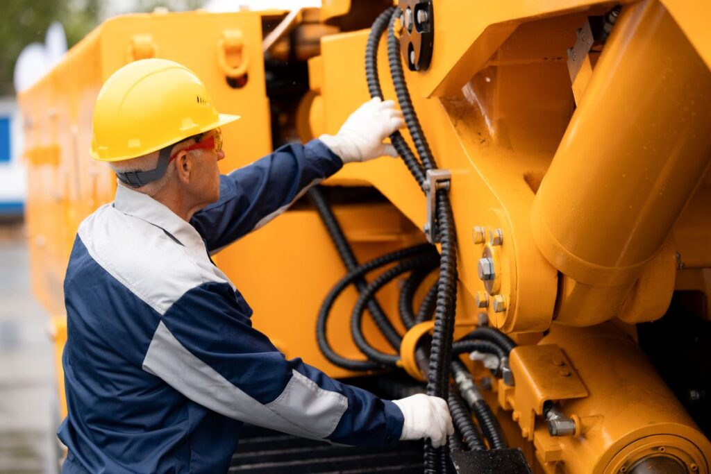 techniker prueft schuetzende ummantelung und verlegung von chemieschlaeuchen an einer hydraulischen industrieanlage