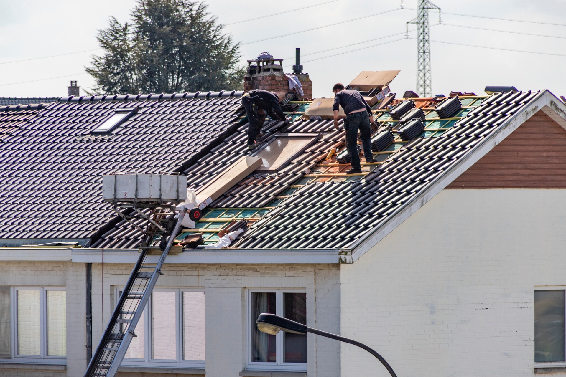 Zwei Handwerker reparieren Ziegeldach mit Förderanlage | Lkw-Arbeitsbühnen mieten

