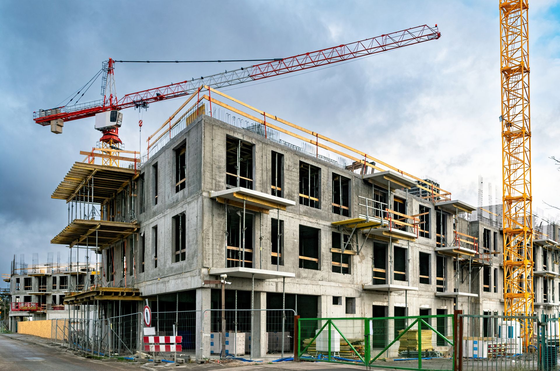 Baustelle mit Rohbau und Kran, abgesperrt durch Bauzäune – städtische Umgebung