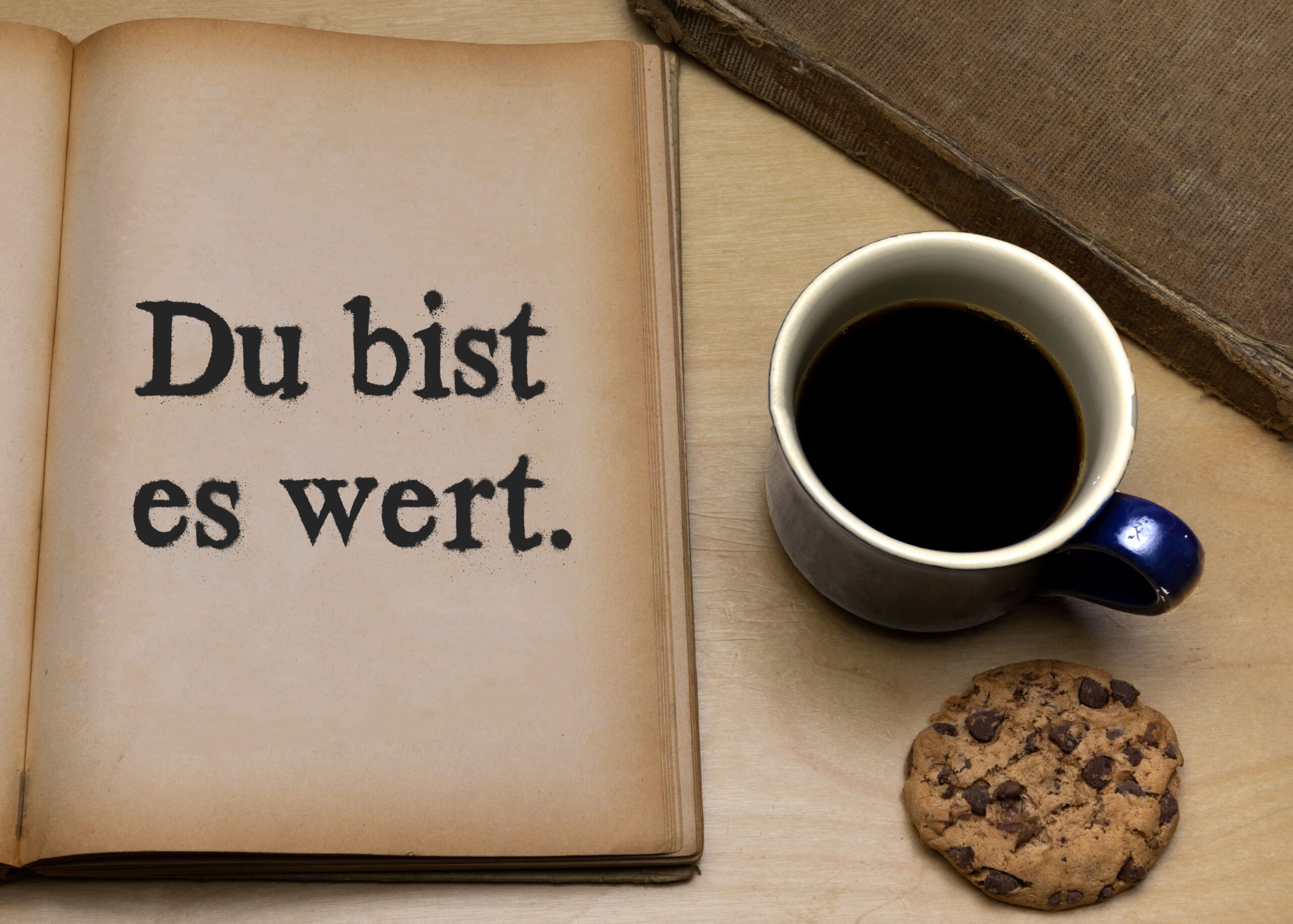 Aufgeschlagenes Buch mit der Aufschrift Du bist es wert, daneben Kaffee und Keks